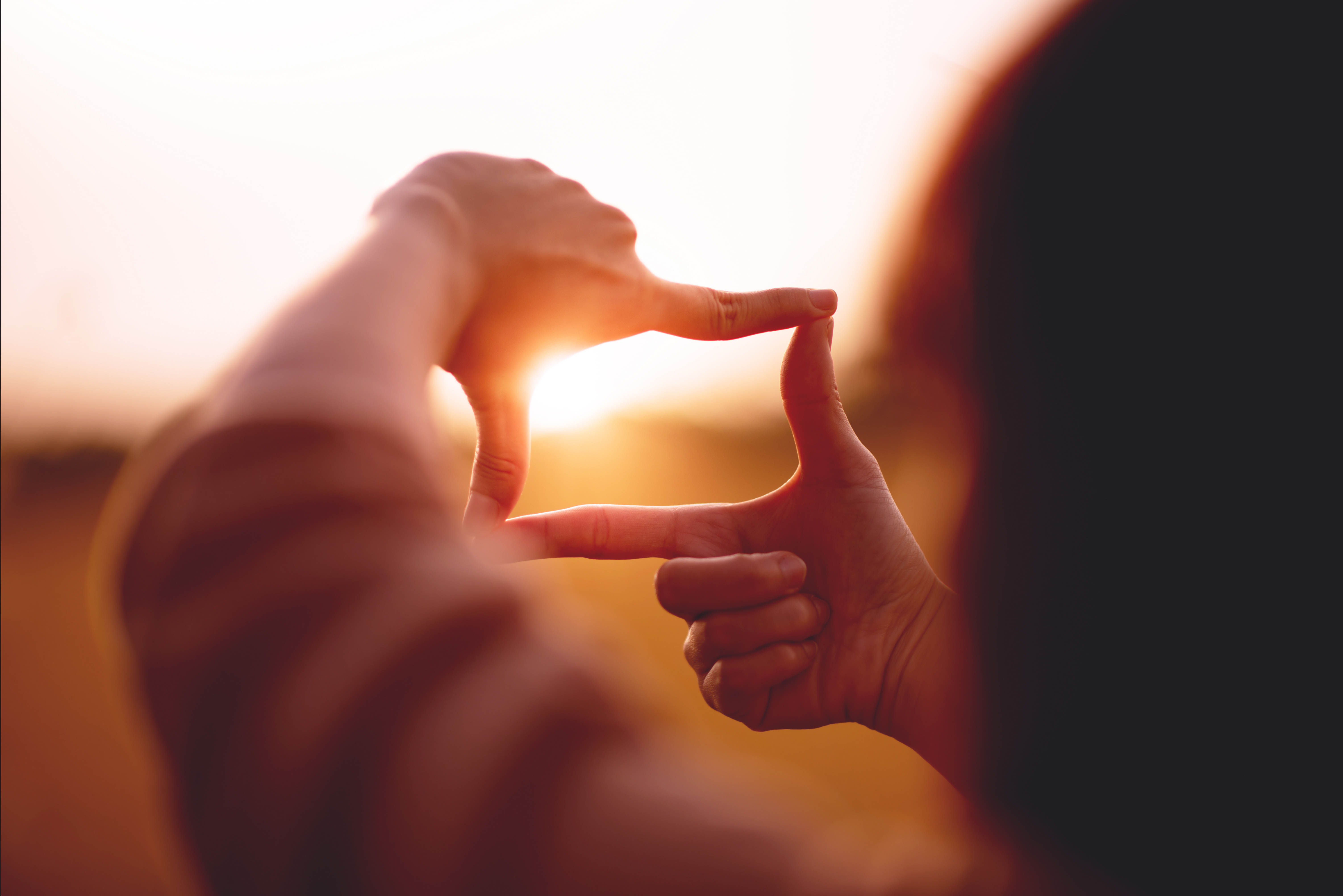 Woman holding up her hands in the shape of a rectangle, framing the sunset in the middle like she's preparing to take a photo Woman holding up her hands in the shape of a rectangle, framing the sunset in the middle like she's preparing to take a photo